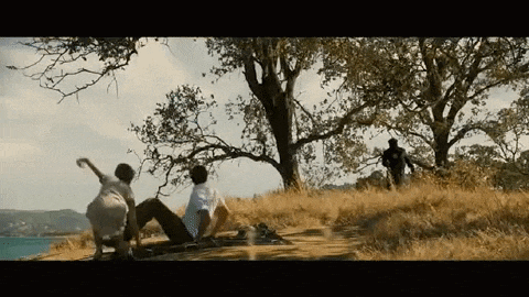 a man and two children are having a picnic on top of a hill near the ocean .