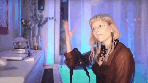 a woman singing into a microphone while standing in front of a white piano