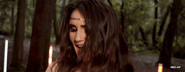 a woman wearing a gold headband is smiling in front of a forest