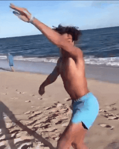 a shirtless man in blue shorts is doing a trick on the beach