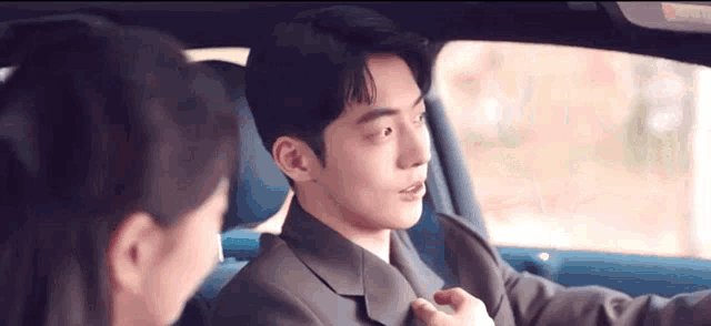 a man and a woman are sitting in a car and the man is adjusting his tie .