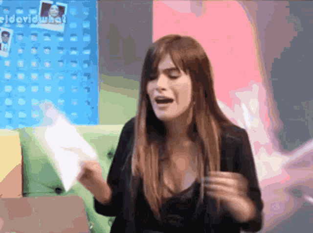 a woman is holding a piece of paper in front of a wall that says " david what "