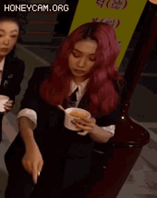 a woman with red hair is holding a cup of soup with a spoon .