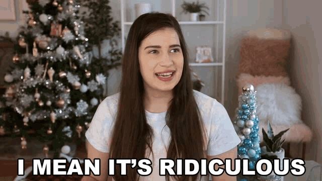 a woman sitting in front of a christmas tree says i mean it 's ridiculous
