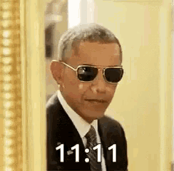 barack obama is wearing sunglasses and a suit and tie while peeking out from behind a picture frame .