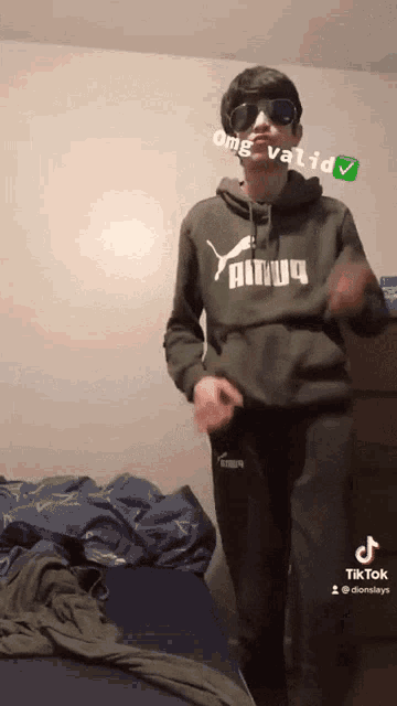 a young man wearing sunglasses and a puma hoodie is dancing in a bedroom