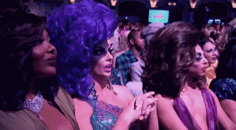a group of drag queens are sitting next to each other in a crowded room .