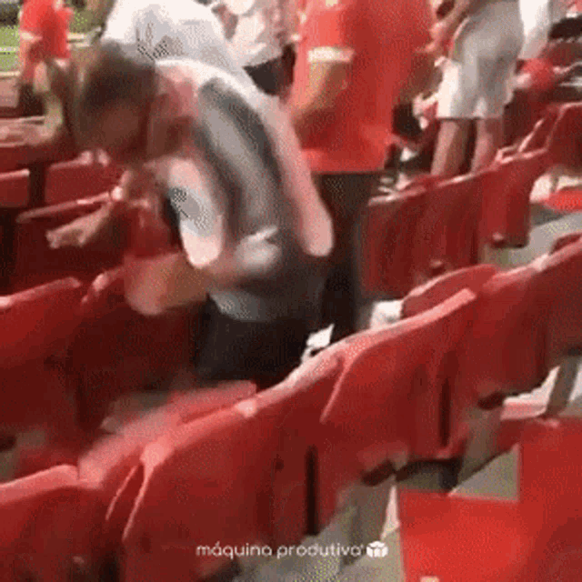 a man in a gray shirt is standing in a row of red seats at a stadium .