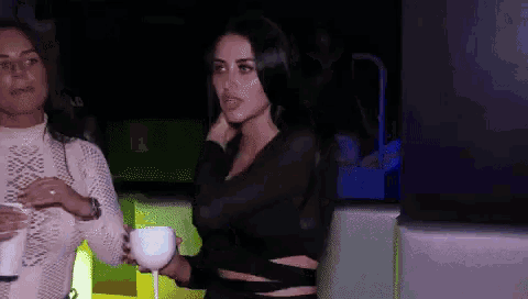 two women standing next to each other with one holding a glass of wine