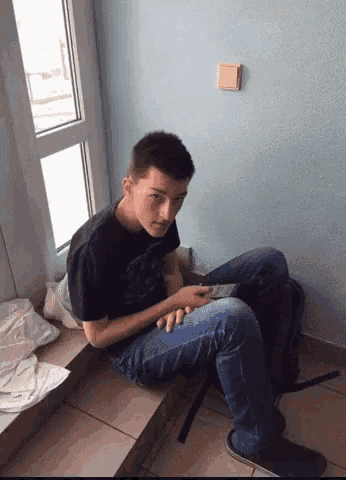 a young man sits on a ledge with his legs crossed looking at his phone