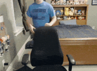 a man in a blue shirt that says ' cube ' on it stands in front of a chair