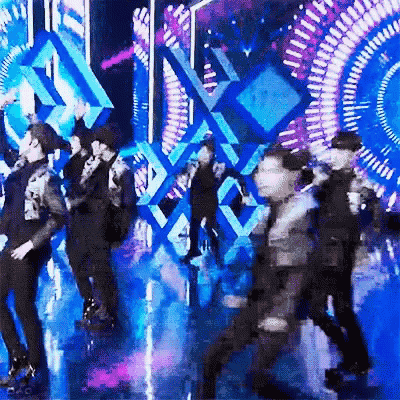 a group of people are dancing on a stage in front of a colorful background