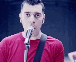 a man singing into a microphone with a guitar strap around his neck