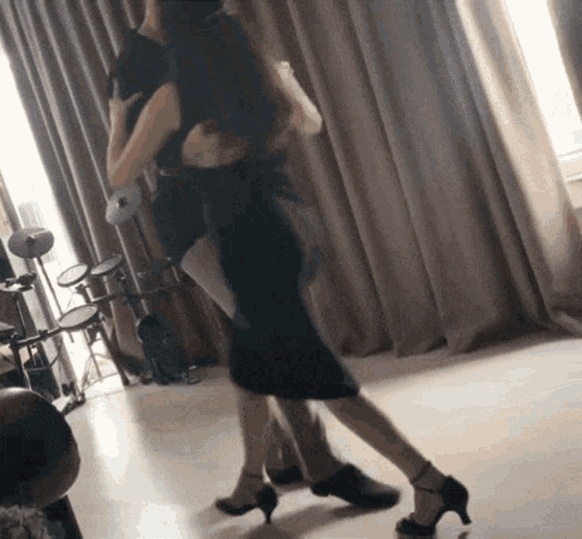 a woman in a black dress is dancing in a room with drums in the background