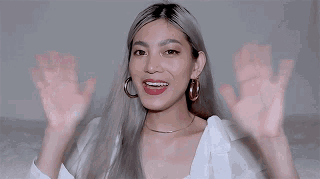 a woman with braces on her teeth and hoop earrings is waving her hands