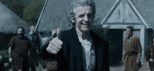 a man in a suit is giving a thumbs up sign while standing in front of a group of people .