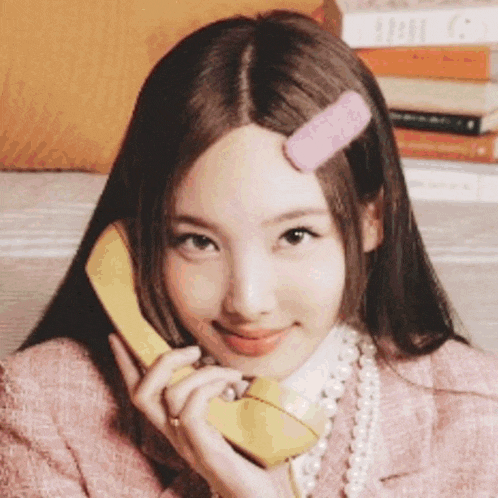 a woman is talking on a yellow telephone with a pink clip in her hair .
