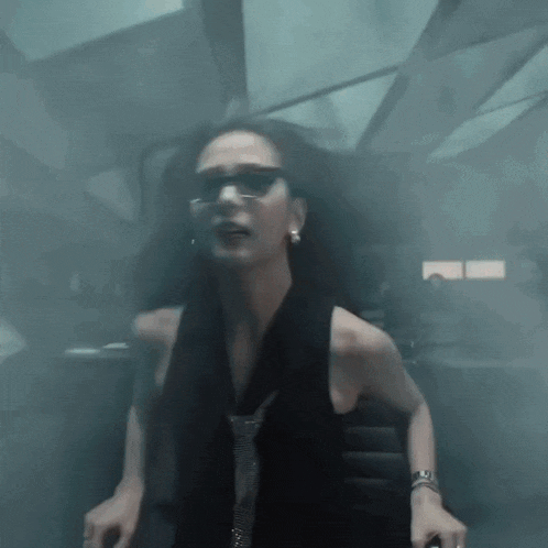 a woman wearing sunglasses and a tie is standing in a dark room