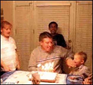 a man blows out candles on a birthday cake while a child looks on