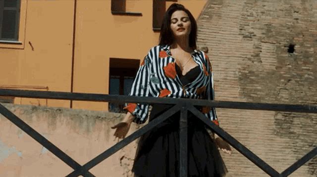 a woman in a striped shirt and black skirt stands on a balcony