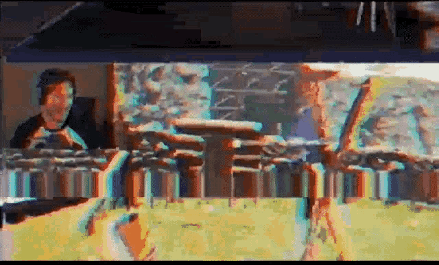 a man is sitting at a table in front of a computer screen with a blurry picture of a field behind him .