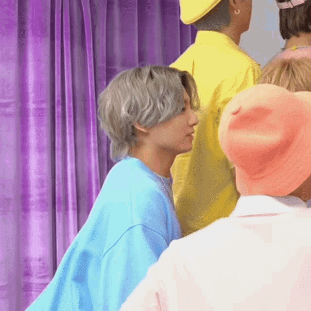 a man in a blue shirt is standing in front of a purple curtain