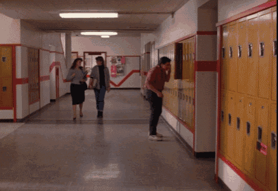 two women walking down a hallway with lockers and a sign on the wall that says ' i 'm sorry '