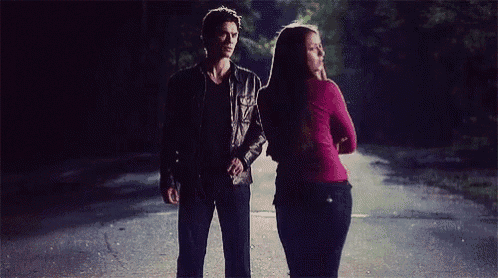 a man and a woman standing next to each other on a road at night .