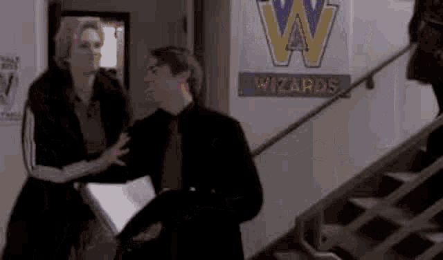 a man and a woman are standing next to each other in front of a sign that says `` wizards '' .