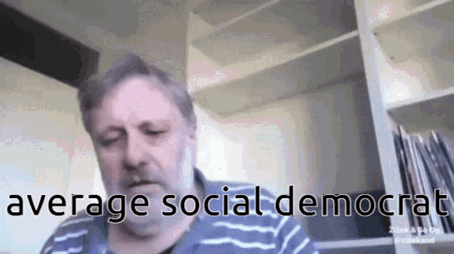 a man with a beard is sitting in front of a bookshelf with the words average social democrat written on the bottom