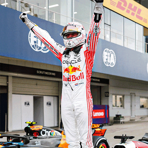 a man wearing a red bull racing suit holds his arms up in the air