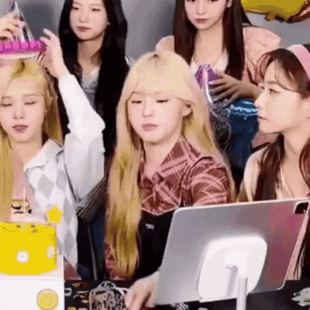 a group of young women are sitting around a table with a computer and balloons .