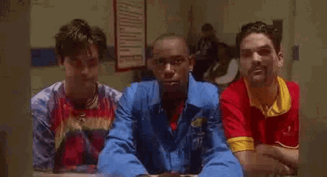 three men are sitting next to each other in a room and making a fist .