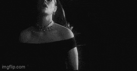 a woman in a black dress and gloves is standing in front of a wall .