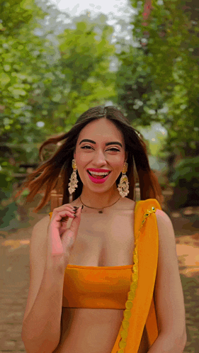 a woman wearing a yellow top and earrings smiles