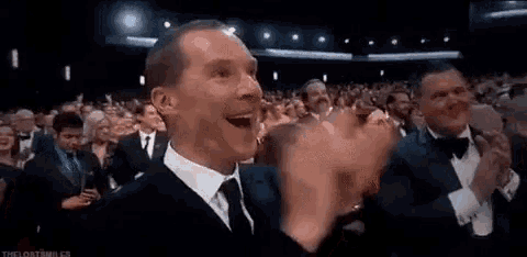 a man in a suit and tie is applauding in front of a crowd of people in a theater .