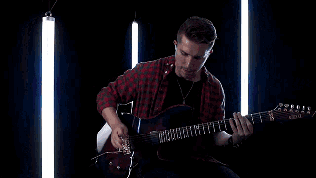 a man in a plaid shirt is playing a guitar that says alvarez on it