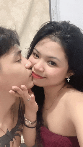 a woman with a cross earring kisses a man 's nose
