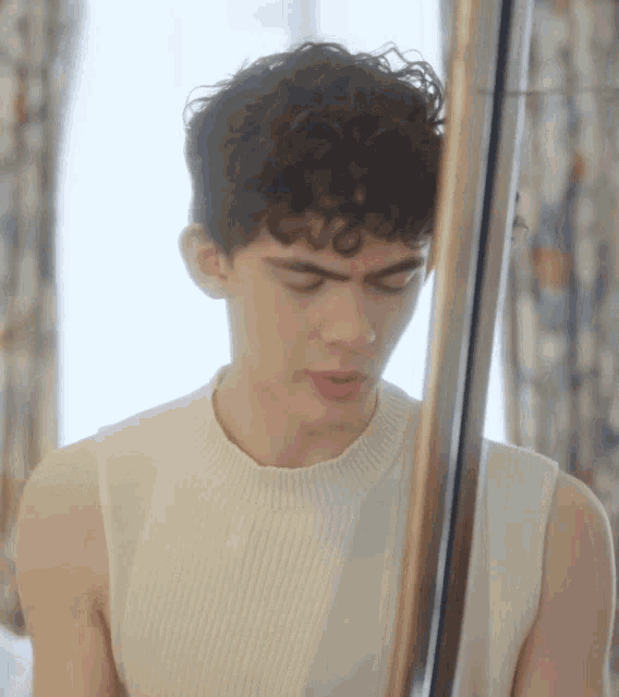 a young man with curly hair is standing in front of a mirror