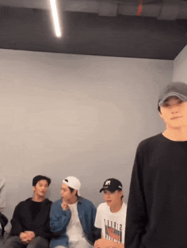 a group of young men are sitting in a room and one of them is wearing a baseball cap with the letter h on it .