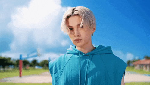 a man wearing a blue sleeveless hoodie stands in a field