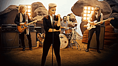 a woman singing into a microphone while a man plays a guitar and another man plays drums