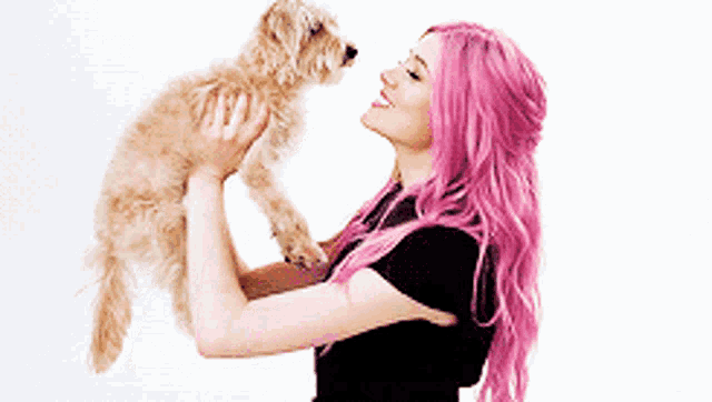 a woman with pink hair holds a small dog in her arms