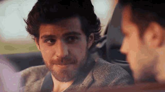 a man with a beard is sitting in the back seat of a car looking at another man .