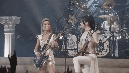 a woman playing a guitar in front of a drum set that says ' mighty ' on it