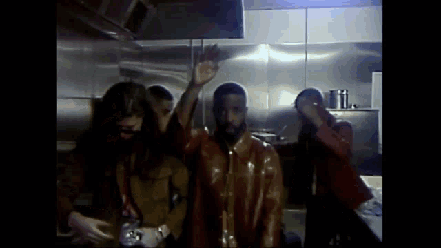 a group of men are standing in a kitchen with their arms up in the air