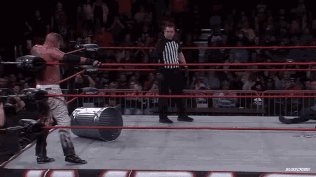 a referee stands in a wrestling ring with a trash can in the middle