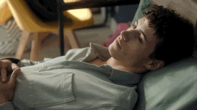 a man with curly hair is laying on a bed with his eyes closed