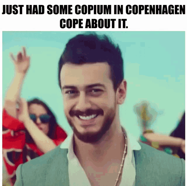 a man with a beard is smiling in front of a group of people with the caption just had some copium in copenhagen cope about it