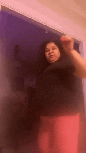 a woman in a black shirt and pink pants is dancing in front of a door .